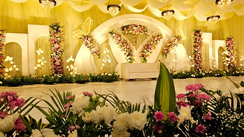Ivory and gold draped stage with floral arch and tropical greens